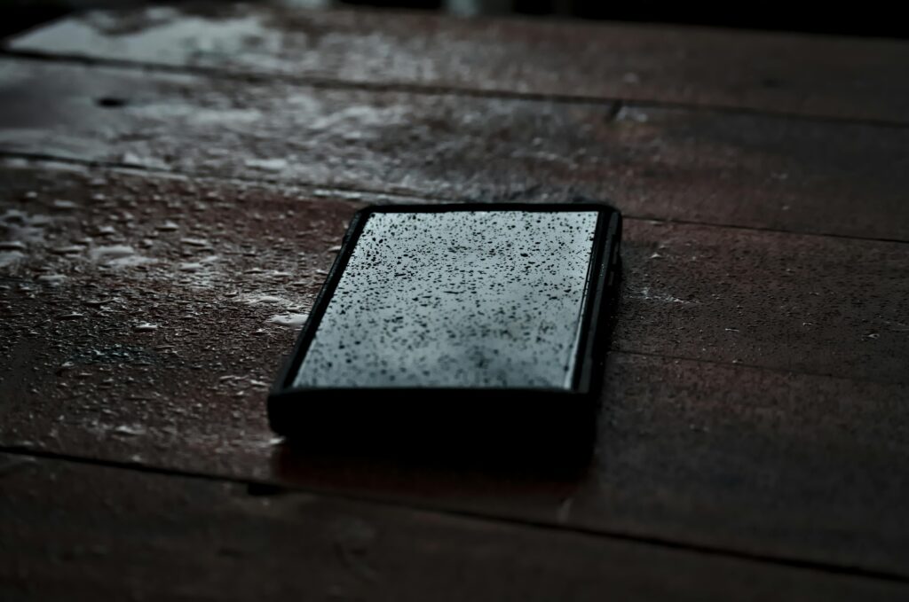 Close-up of a smartphone with droplets on a wet wooden surface, emphasizing waterproof technology.